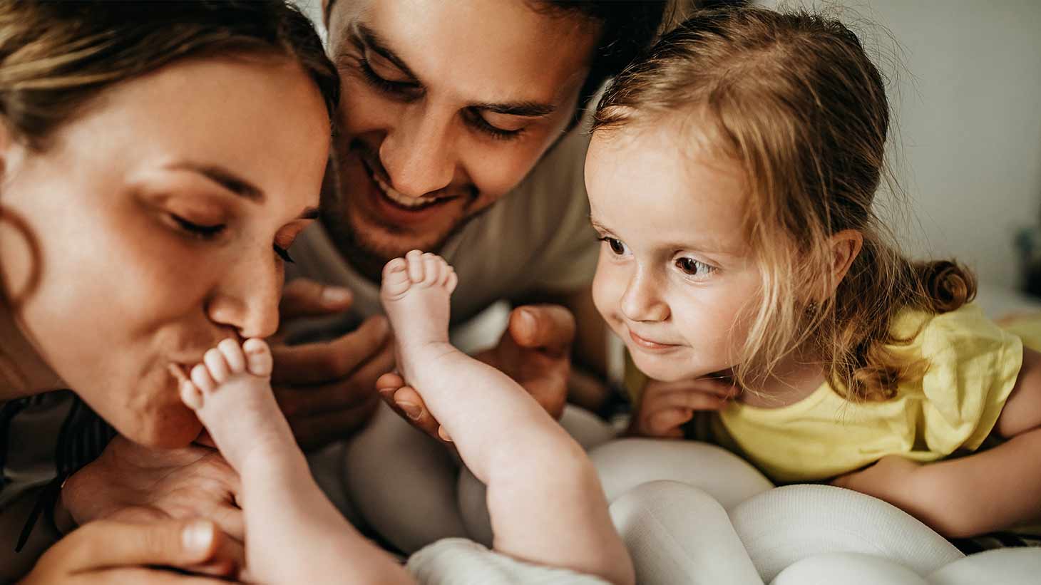 Una pareja besa los pies de un bebe recostado junto a una niña pequeña